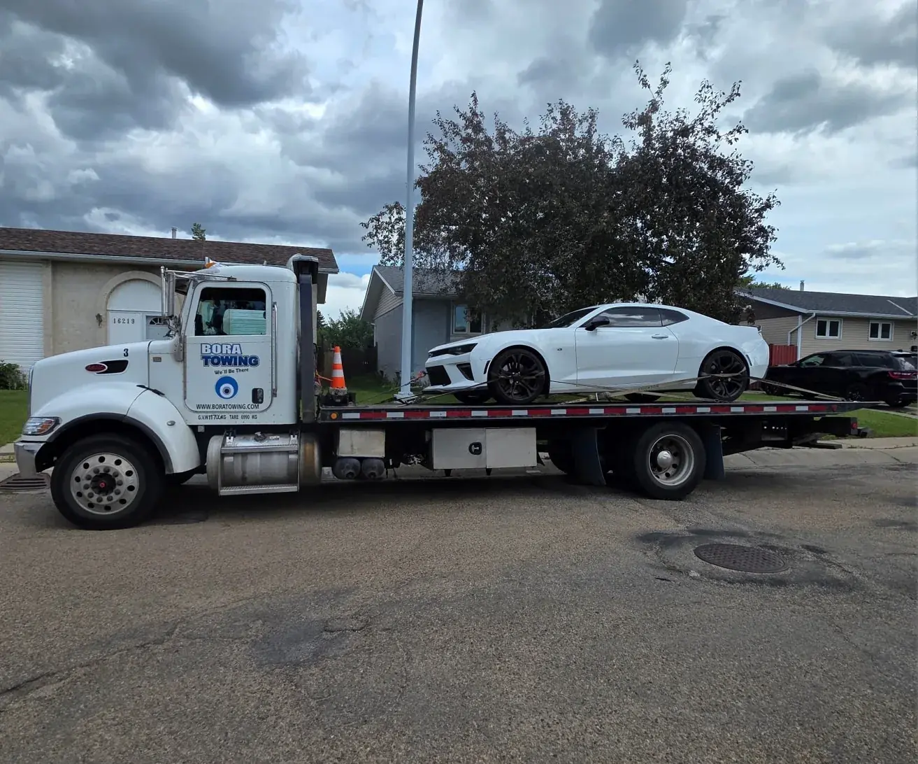 Bora Towing flatbed transporting a white Chevrolet Camaro in an Edmonton residential area